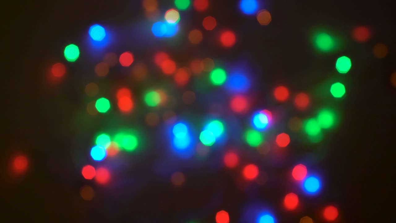 Bright multicolored blurred lights of the garland flash on the dark background. Preparation of the holiday. Festive illumination. Close-up. 4K.