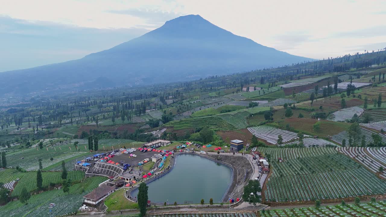 Aerial scenery of water reservoir and plantation with mountain background in the morning. Indonesia nature rural landscape.