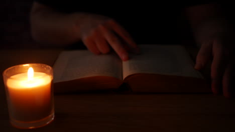 a man reading a book by candlelight in a dark room