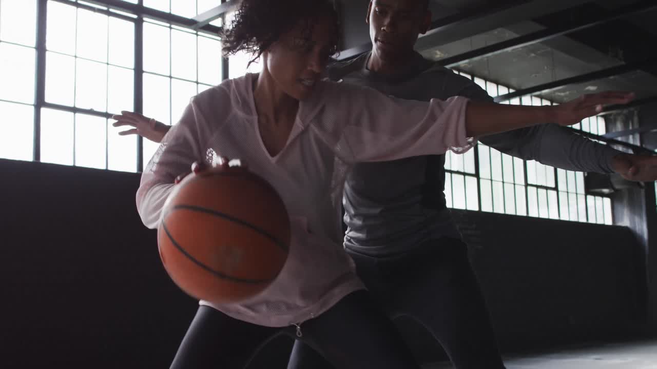 African american man and woman standing in an empty building playing basketball