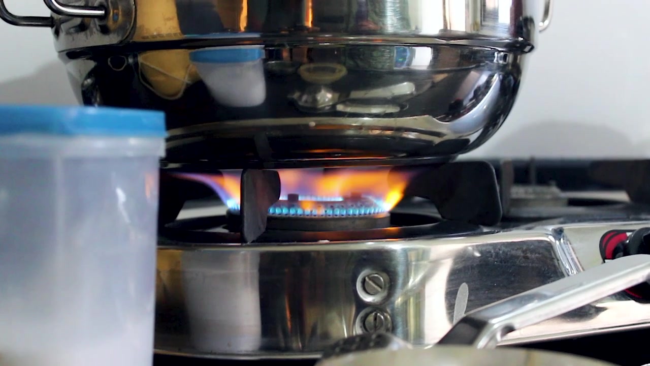 Primo piano dettagliato di una fiamma di fornello a gas che riscalda pentole durante la cottura casalinga, ideale per progetti di cucina, preparazione dei pasti, culinaria, energia e stile di vita domestico.