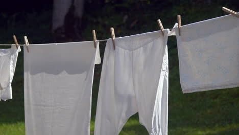 panning shot of white laundry drying outdoors on clothesline between trees in garden ,close up