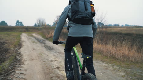 Cyclist-With-Backpack-Riding-A-Mountain-Bike-Down-The-Road-In-The-Countryside