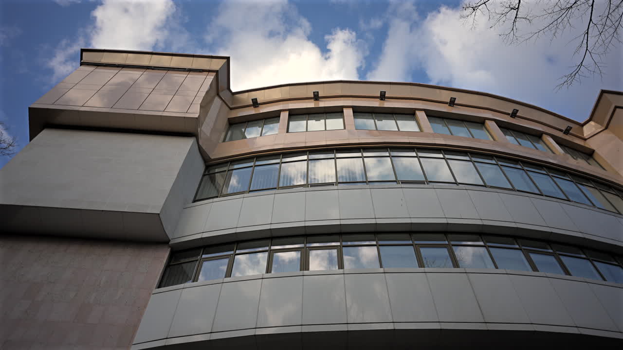 Vista dal basso della facciata di un moderno edificio per uffici con finestre di vetro e architettura curva contro il cielo