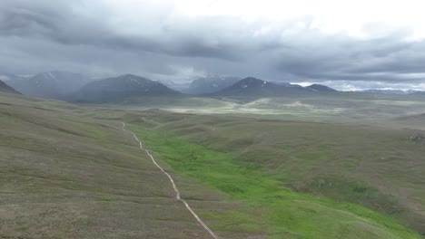 Drone-footage-over-a-green-field-valley-in-the-mountains-of-Pakistan,-Deosai-Skardu-on-a-cloudy-day-while-raining