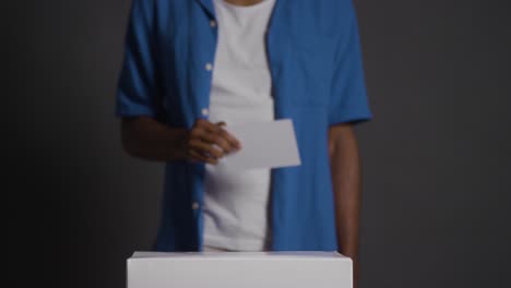 close up of man casting vote into election ballot box against black background 2