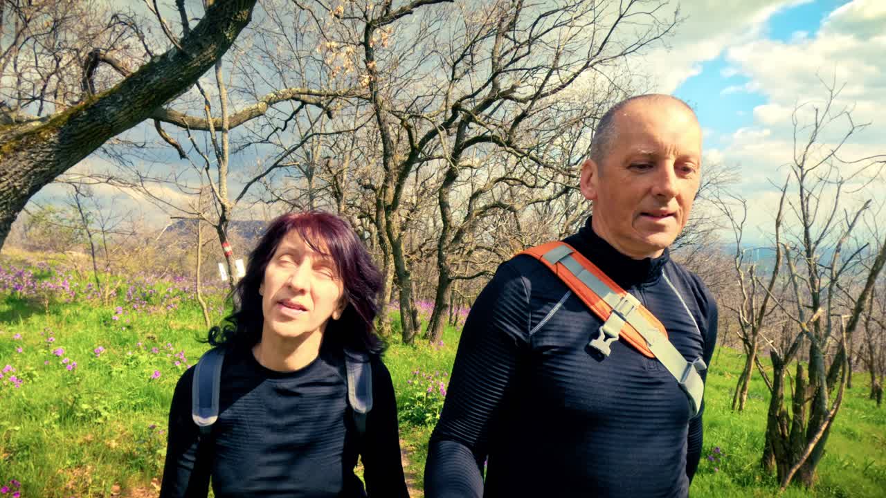 Pareja sonriente explorando un pintoresco sendero forestal cubierto de flores. Destacando la alegría de la compañía, los intereses compartidos, el amor y la felicidad al aire libre