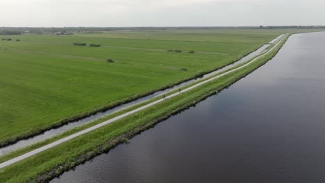 biking along the tranquil canal and green fields in netherlands. - aerial shot