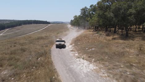 vehículo del ejército de israel conduciendo a través del campo verde en la carretera rural del campo de entrenamiento, tiro de seguimiento aéreo