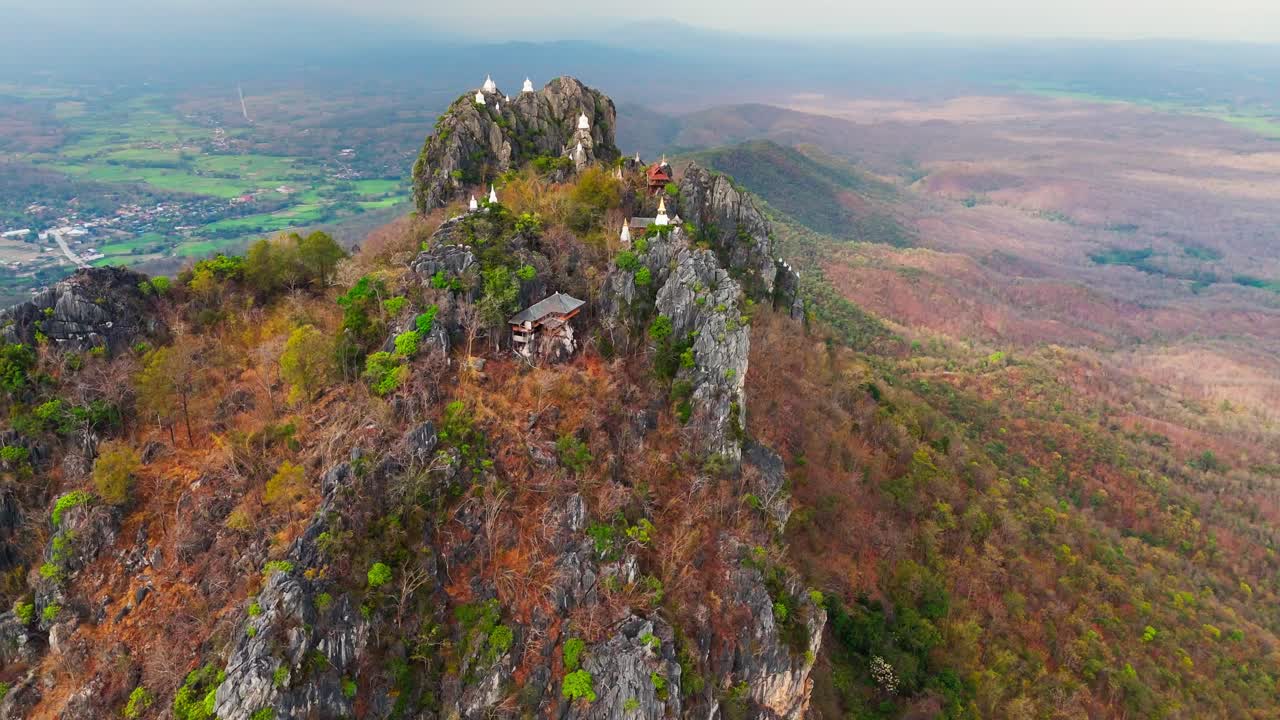 Sacred Wat Chaloem Phra Kiat temple on rocky mountain peak under cloudy afternoon sky, orbit establish