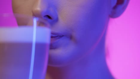 close up of a young woman drinking a delicious vegan coffee latte machiato or cappuccino and then licking her lips with her tongue and being happy in slow motion against a purple background