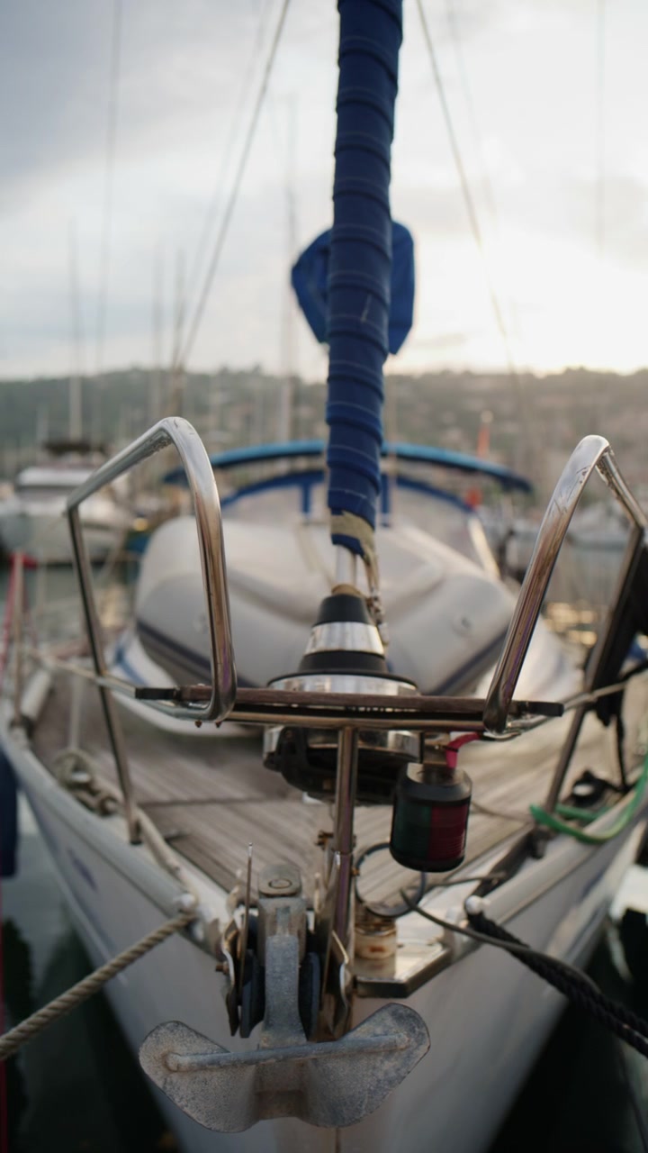 Vista ravvicinata della poppa di una barca a vela con sartiame avvolto in blu, ancora, attrezzatura di coperta e riflessi del porto turistico a Port Vauban ad Antibes, Francia.