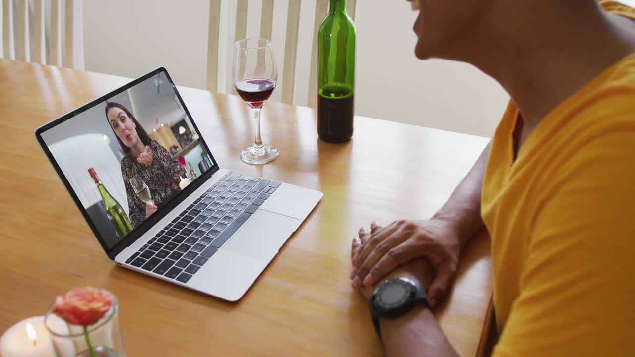 Mid section of african american man with wine while having a video call on laptop at home