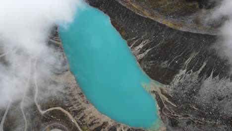 Top-down-view-of-a-turquoise-lagoon-surrounded-by-clouds-next-to-a-road-in-Huaraz-Peru