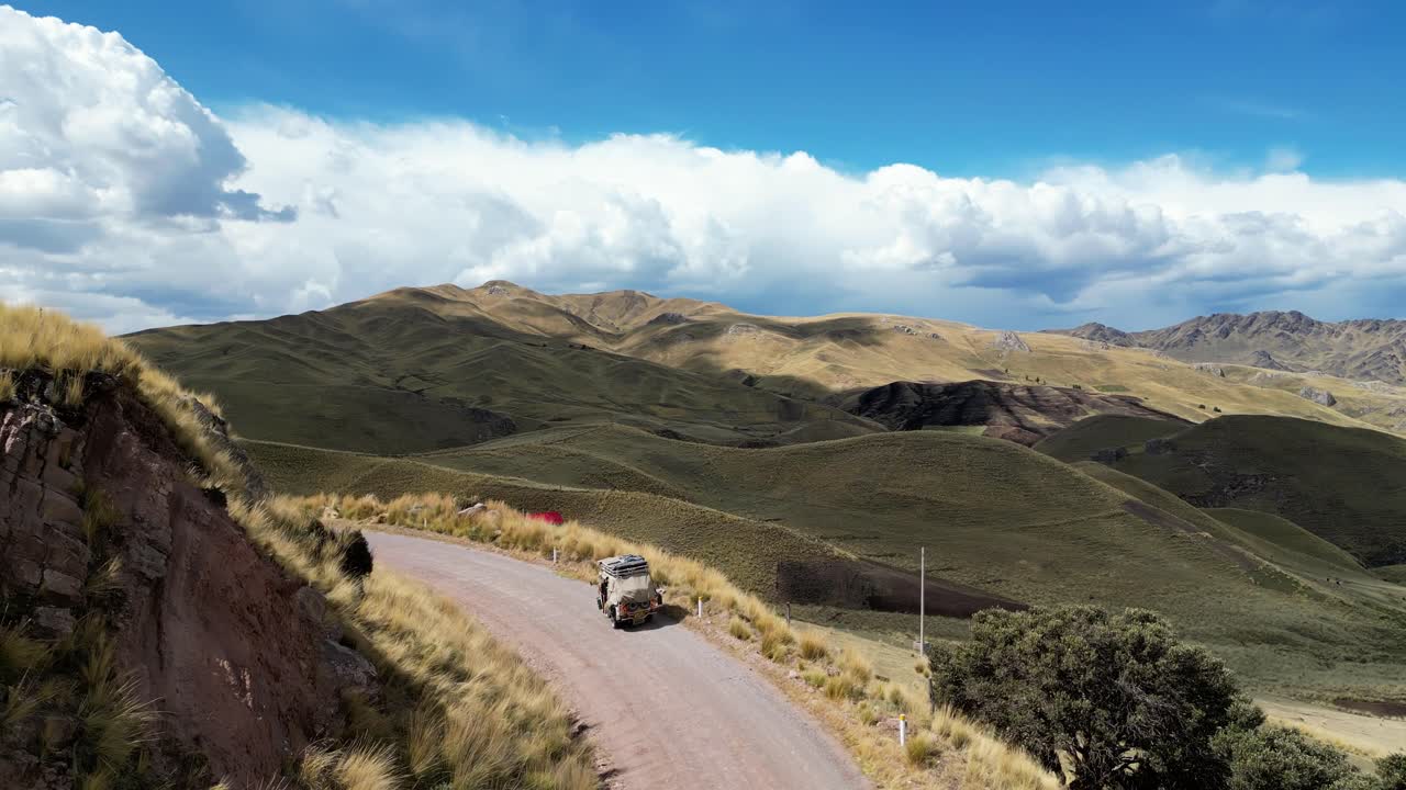 4K drone reveal of a tuk tuk crossing a grassy valley, sunlight painting the fields gold and green under a vast sky