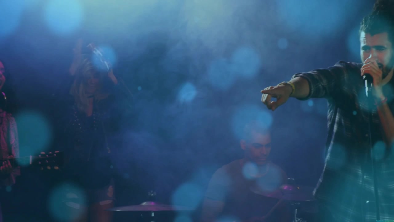 Cantante principale che entra nell'inquadratura, afferrando il microfono e cantando, coinvolgendo i fan, con bokeh blu sul palco musicale.