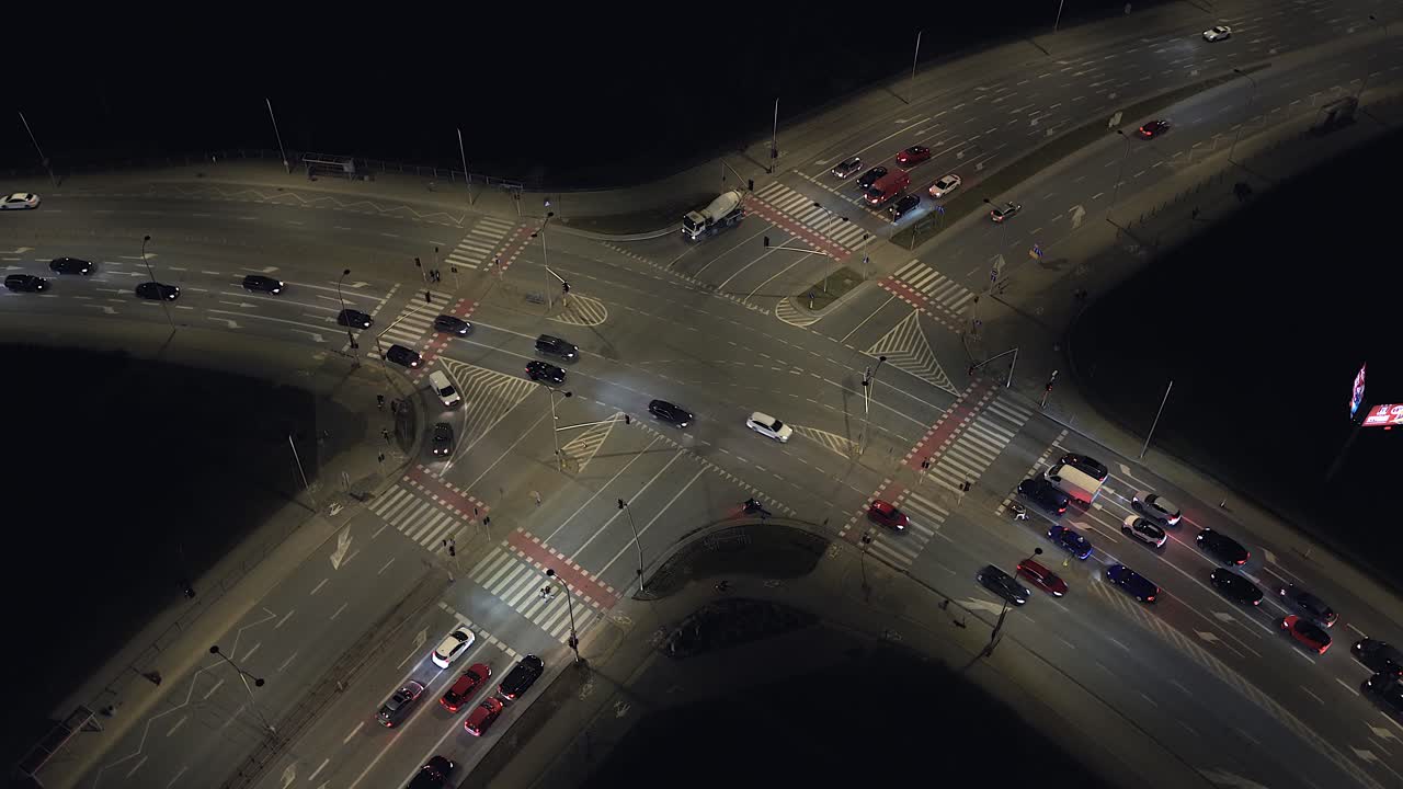Rotating aerial perspective of a bustling road intersection in warsaw, poland. Cars with headlights on move through the illuminated streets at night