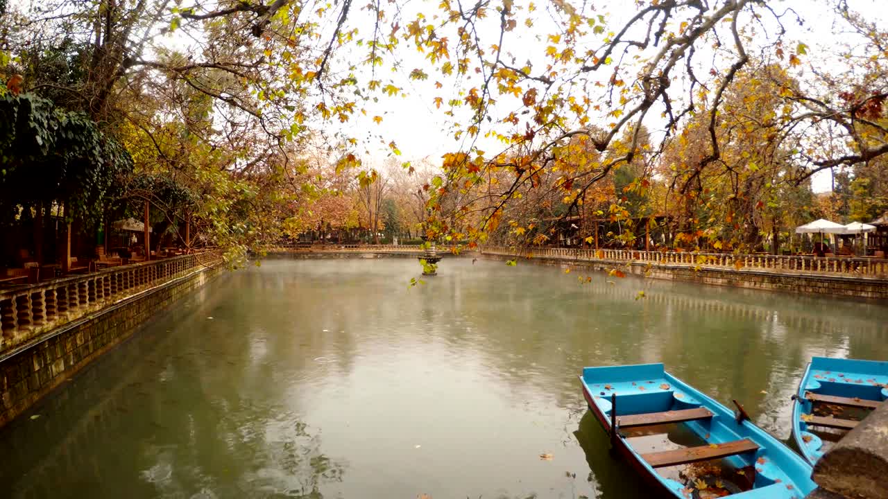 두 개의 파란색 보트 모어 안개는 푸른색과 노란색 나무 주변의 분수와 연못 아래에 떠 있습니다.