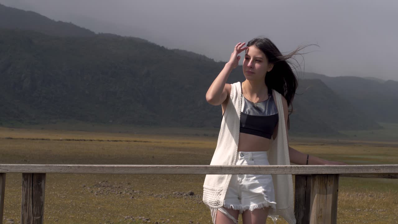 Girl in black crop top and white cardigan adjusts hair blowing in wind at cotopaxi national park