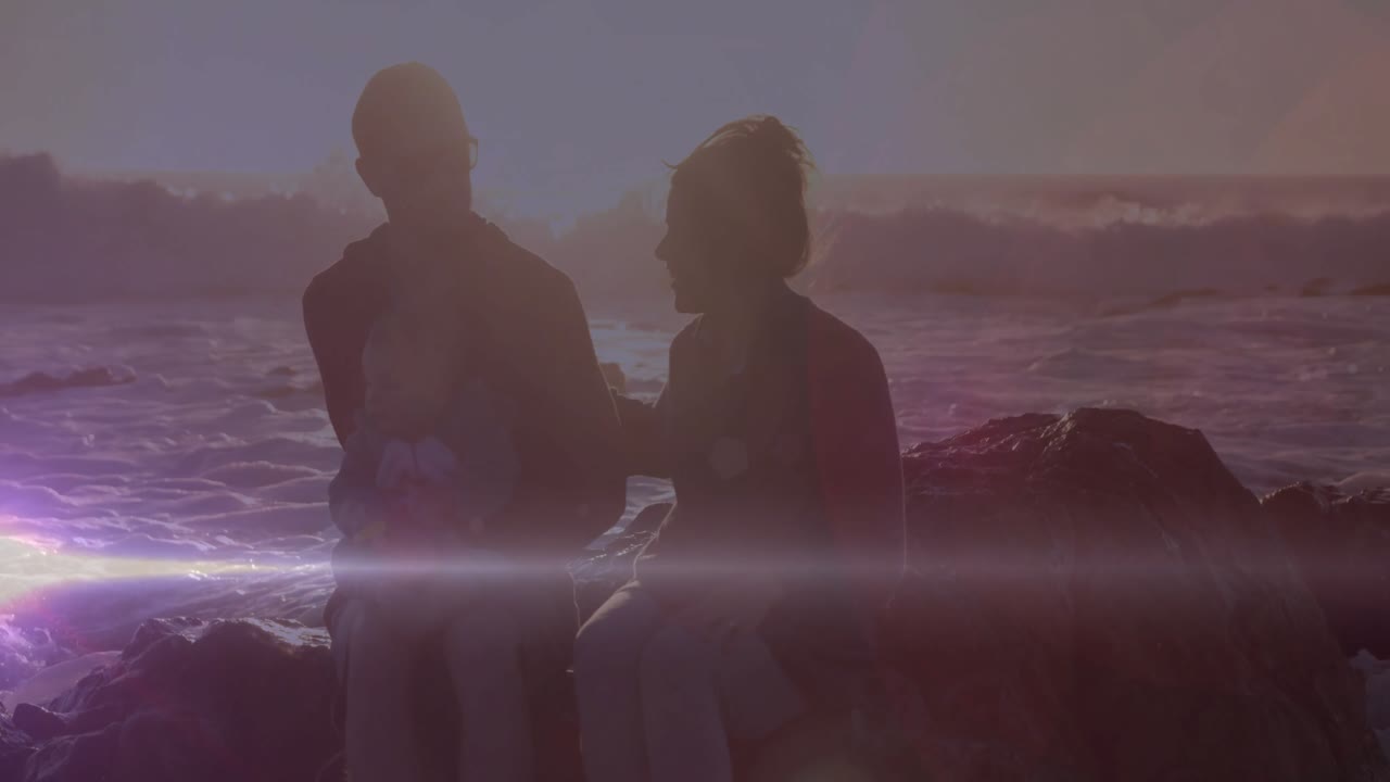 Viajantes sentados na praia ao pôr do sol, mulher colocando a mão no ombro, tranquilizando o homem que contempla o horizonte.