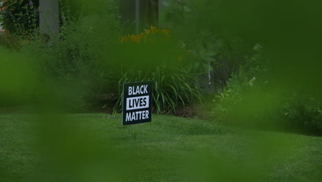 „Black-Lives-Matter“-Schild-In-Einem-Vorgarten,-Von-Der-Anderen-Straßenseite-Und-Durch-Einen-Busch-Aus-Gesehen