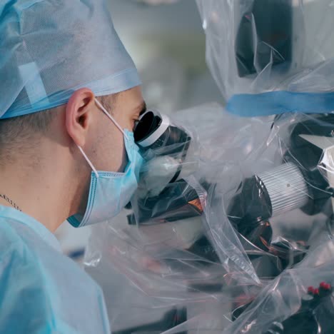 specialist looking into medical microscope. surgeon in blue uniform performing an operation through the modern microscope in surgery room.
