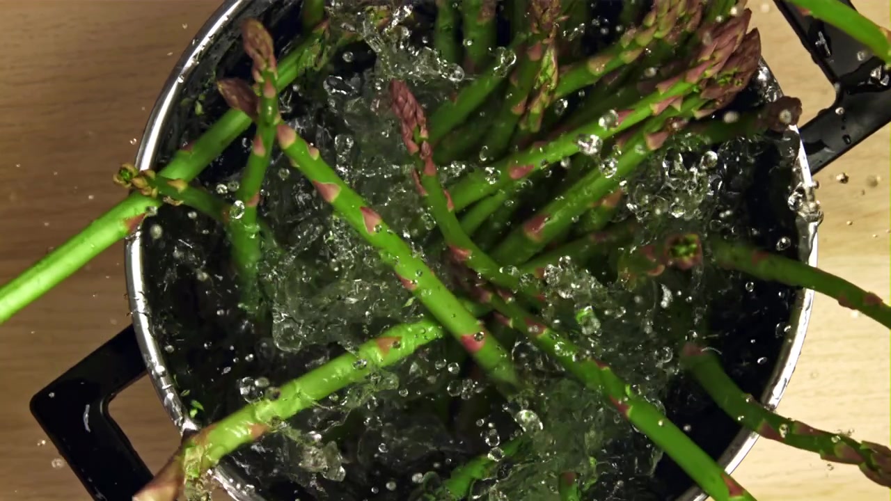 Asparagi verdi freschi che cadono in acqua bollente al rallentatore