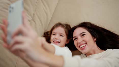 Mother-and-daughter-taking-selfie-at-home-while-lying-on-bed