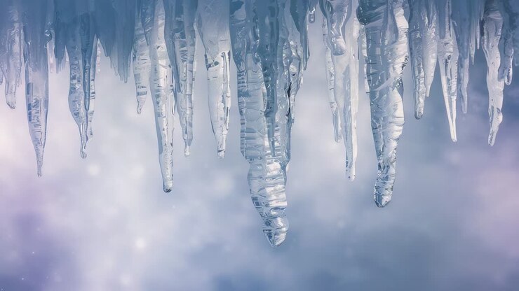Dripping icicle cluster reacting to slight warming, releasing lengthening droplets on roof overhang