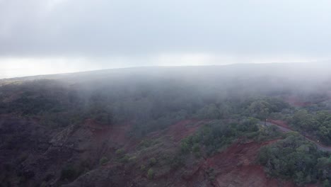 Toma-Aérea-Descendente-Baja-Volando-A-Través-De-Espesas-Nubes-Hacia-Una-Carretera-De-Montaña-Cerca-Del-Cañón-Waimea-En-Kaua&#39;i,-Hawai&#39;i