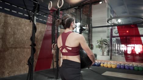 mujer trabajando con una pelota de medicina en un gimnasio