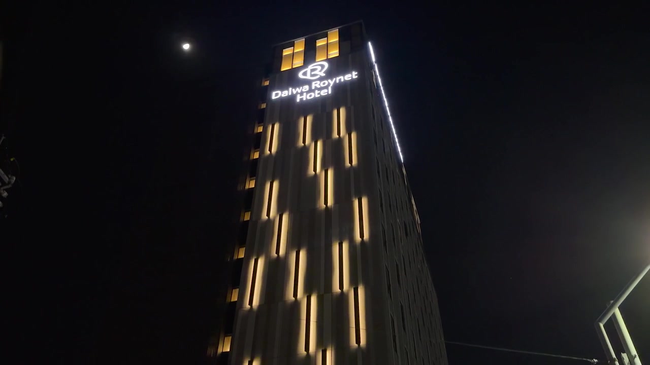Plano inclinado de baixo ângulo da fachada iluminada de um hotel e de uma loja de conveniência à noite no Japão.