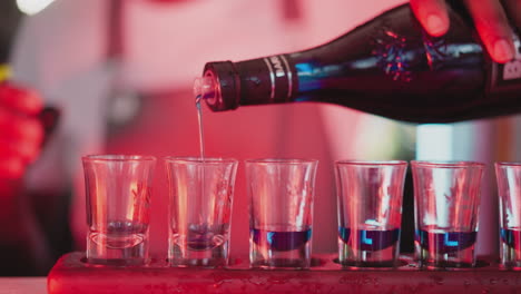 barman giet likeur in kleine glazen op de toonbank close-up. bartender creëert shot sets voor feestgasten in nachtclub. feestelijke sfeer in bar