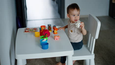 beautiful toddler sits at little table playing with toys. baby studying animals and colors.