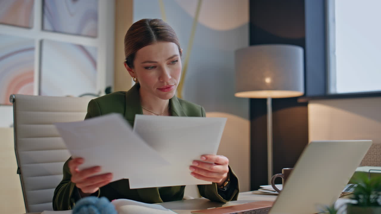 Serious creator looking papers sitting laptop table in office interior closeup