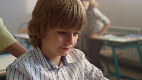 smiling schoolboy siting at desk in school class. male student looking down