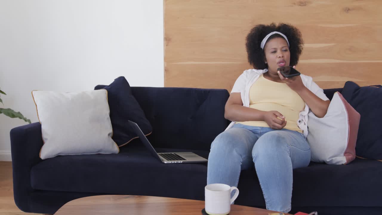 African american plus size woman sitting on sofa and talking on smartphone, unaltered, slow motion