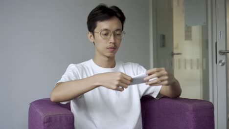 Asian-man-sitting-down-on-a-purple-chair-and-reading-from-a-piece-of-paper-for-an-interview-and-speaking