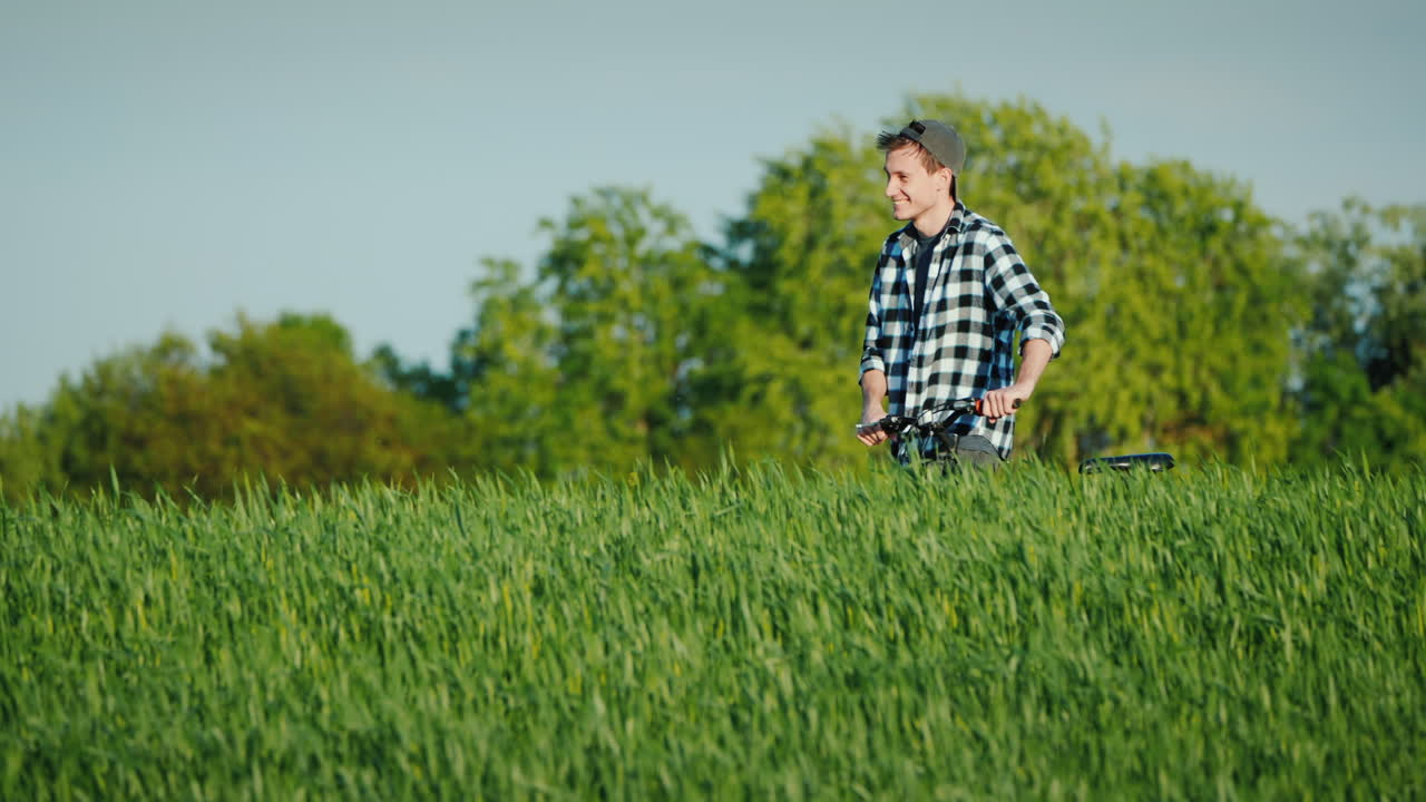 웃고 있는 청년이 자전거를 타고 밀밭 사이의 그림 같은 지형을 걷고 있다