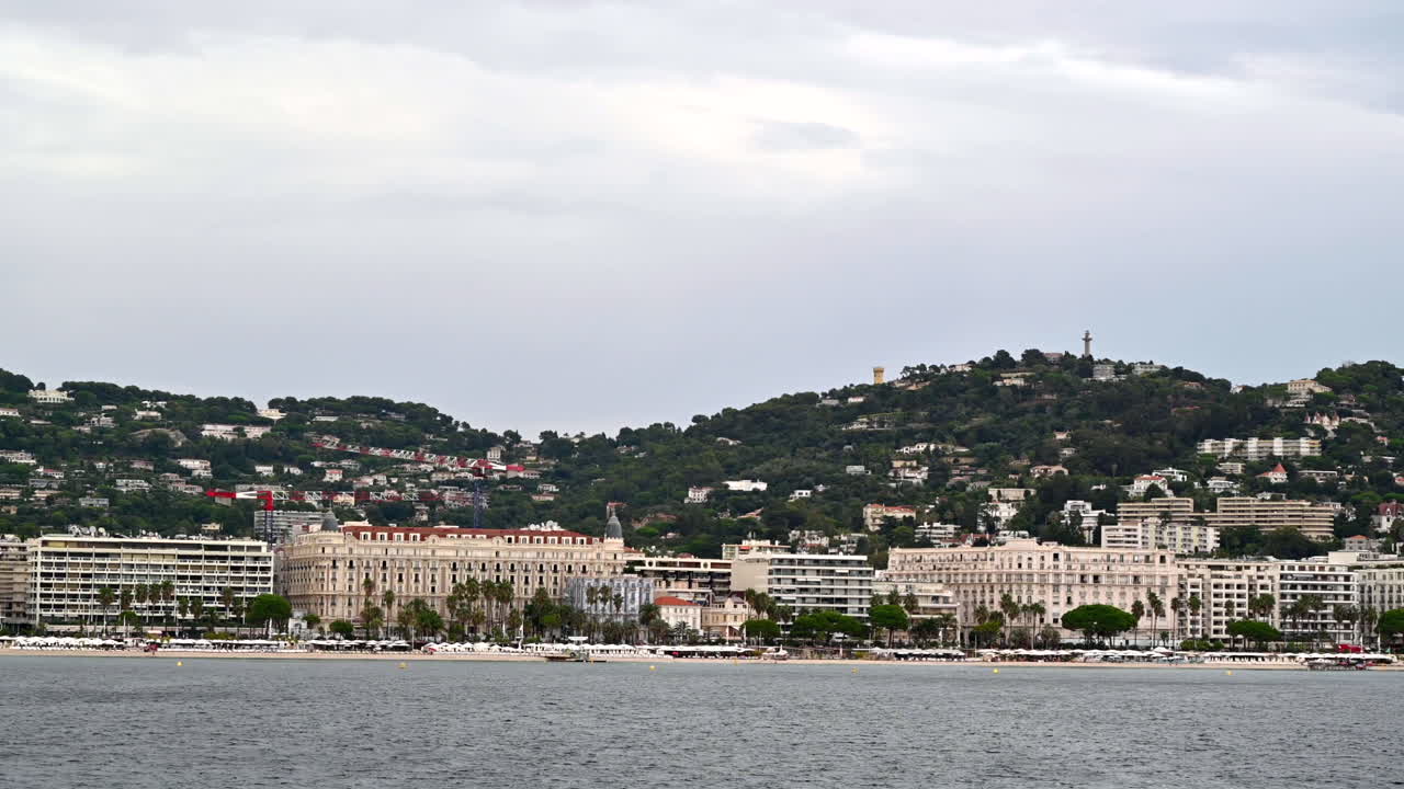 View of Cannes from a floating boat, France. Multiple buildings made in traditional style, greenery, beach