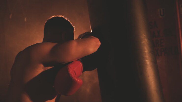 Pugile a torso nudo che riposa appoggiato al sacco da boxe