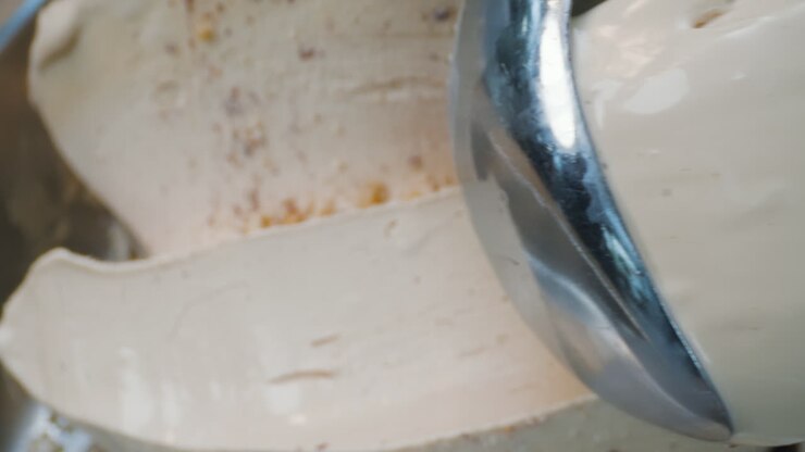 A close-up of a creamy hazelnut ice cream infused with eucalyptus being scooped out using a metal scoop. It has a smooth texture, herbal aroma, and an artisanal look.