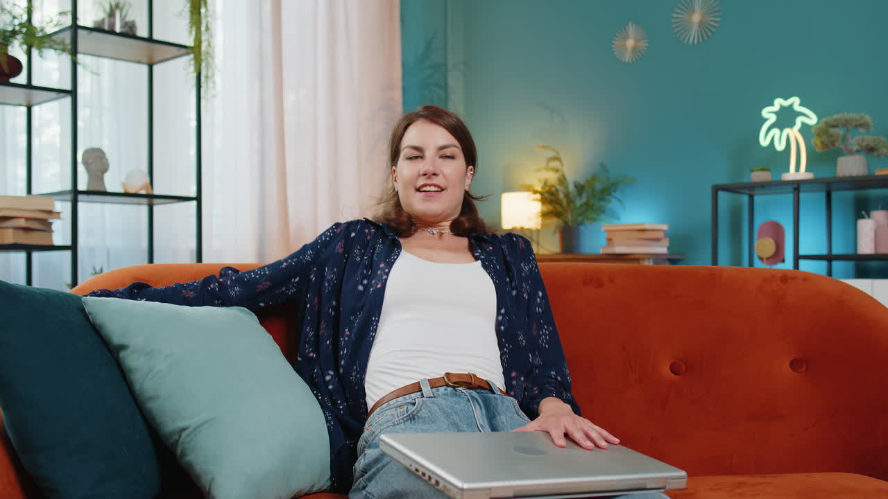 Happy caucasian young woman sitting on couch closing laptop after finishing work relaxing at home