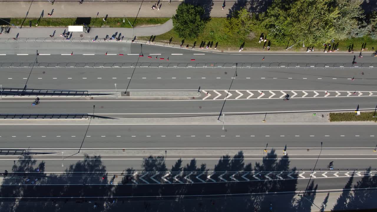 Aerial drone footage captures cyclists participating in the tallinn triathlon, showcasing an urban road with spectators lining the route on a sunny day
