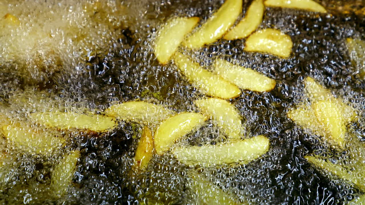 Crispy potato in boiling oil. Bubbles of hot oil during cooking french fries in deep fryer. Process of cooking golden fried potatoes. Macro shot.