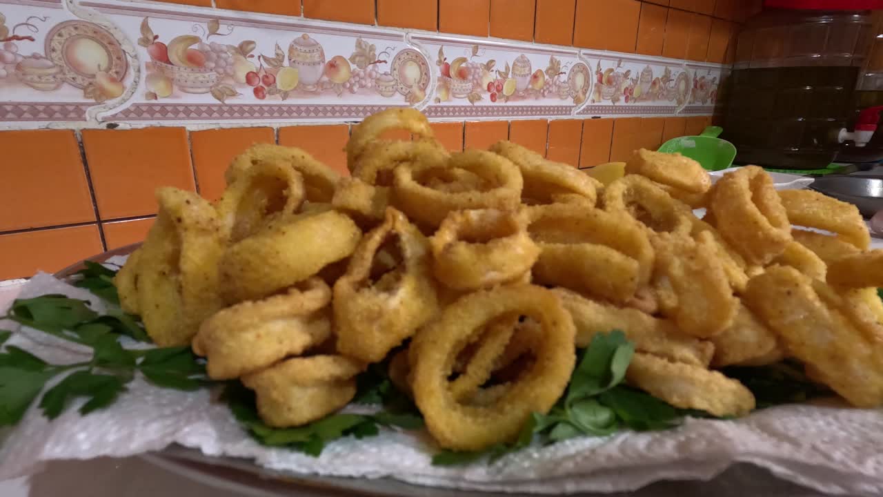 Piatto di anelli di calamari dorati fritti ricoperti di pastella condita, sollevati con un mestolo forato, che mostrano un antipasto di pesce croccante, uno snack tradizionale in stile marocchino e una consistenza croccante.