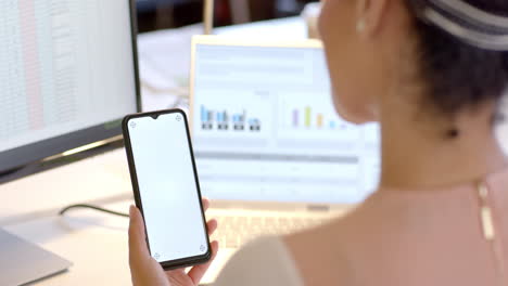 mujer de negocios caucásica usando un teléfono inteligente con pantalla en blanco y una computadora portátil en la oficina con espacio para copiar