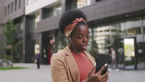 young businesswoman with earphones looking at smartphone screen during communication in urban environment