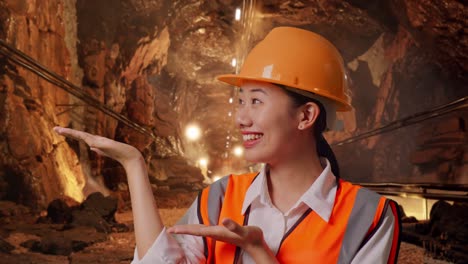 close up of asian female engineer with safety helmet smiling and pointing to side in underground mine tunnel