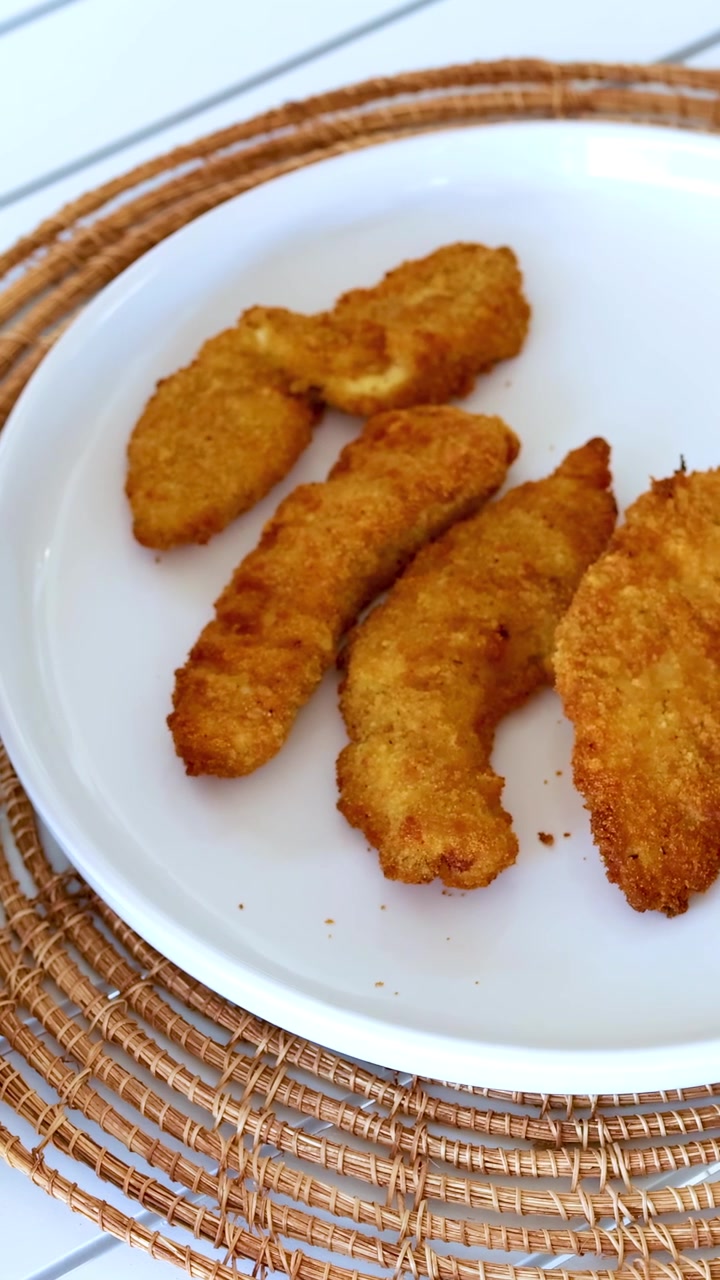Strisce di pollo dorate vengono rimosse da una friggitrice ad aria e posizionate su un piatto in un ambiente cucina luminoso.